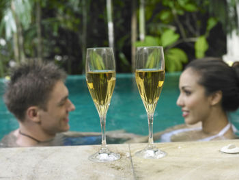 Close-up of drink at poolside with couple in swimming pool