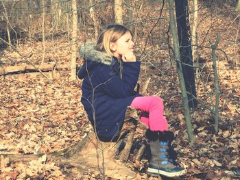 Thoughtful girl sitting on tree stump in forest during autumn