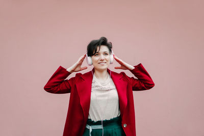 Young beautiful woman in pink headphones listening to music on pink wall background. young gen z 