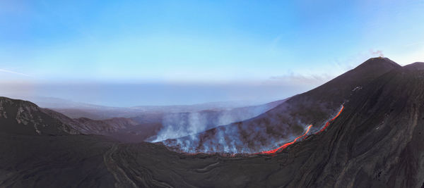 Etna erupting top view with lava flow and smoke-blue sky during blue hour- aerial panorama at sunset