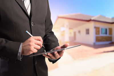 Midsection of businessman using digital tablet in city against sky