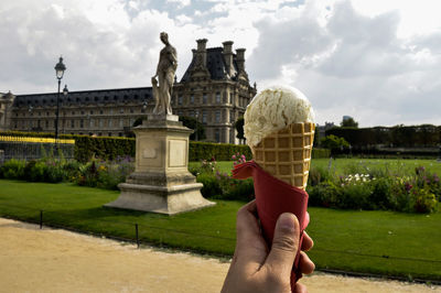 Cropped hand holding ice cream against musee du louvre