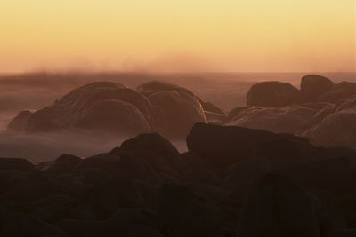 Scenic view of rocks at beach against sky during sunset