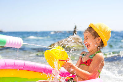 Girl playing with water on beach against sky