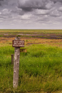 Information sign on wooden post on field against sky