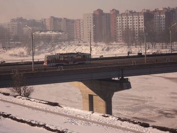 Bridge over frozen river in city against sky during sunset