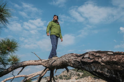Frontal view of man standing on tree against sky