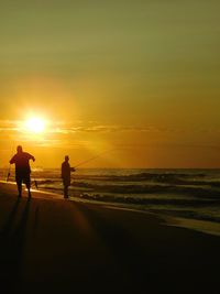 Silhouette people on beach against sky during sunset