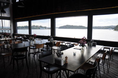 Empty chairs and tables in restaurant by sea against sky