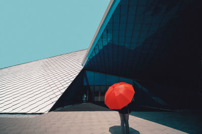 Person with umbrella standing by building against clear sky