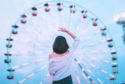 Rear view of woman gesturing peace sign while standing in amusement park