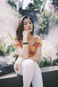 Thoughtful young woman sitting by plants in park