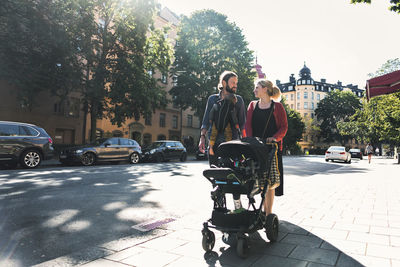 Mid adult parents with baby boy and stroller walking on sidewalk in city