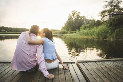 Rear view of couple sitting on lake against sky