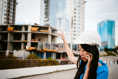 Young woman using mobile phone in city against sky