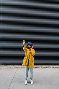 Woman with arms raised watching video through wearable computer while standing against wall