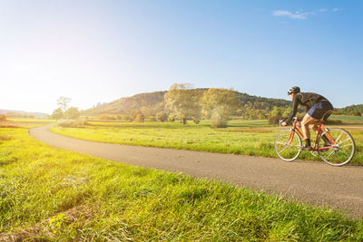 Man riding bicycle on field against sky