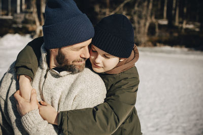 Affectionate father and son wearing knit hat embracing each other on sunny day
