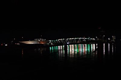 Illuminated bridge over river against sky in city at night