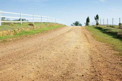 Dirt road amidst field against sky