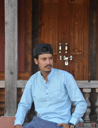 A good looking indian young guy with wearing cap backwards, looking sideways while sitting in temple 