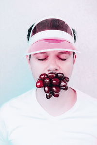 Close-up of young man with fruit in mouth against white background