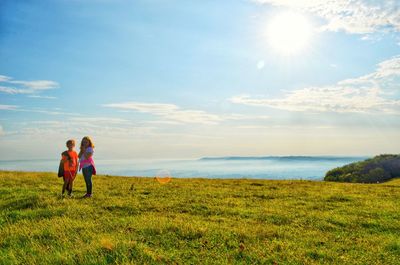 Siblings standing on grassy land against blue sky