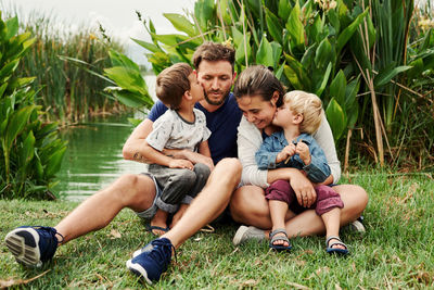 Full length of happy family sitting by pond