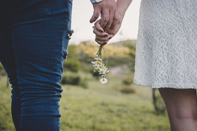 Midsection of couple holding hands and flowers