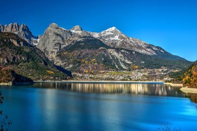 Scenic view of lake and mountains against clear blue sky
