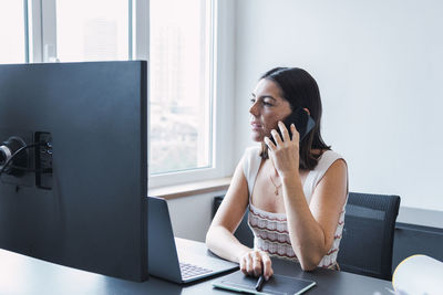 Young businesswoman talking through smart phone in office