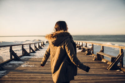 Rear view of woman standing at beach against sky