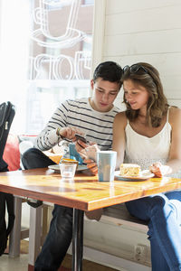 Couple using mobile phones while sitting at restaurant table