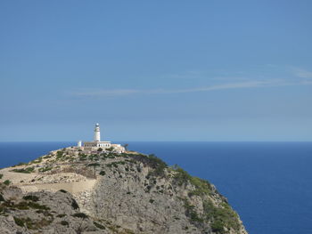 Lighthouse by sea against blue sky