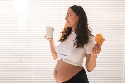 Young woman holding ice cream standing against wall