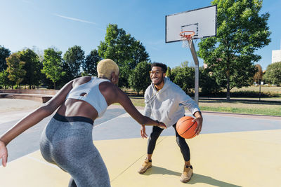 Smiling sportsman playing basketball with friend in sports court