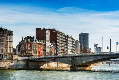 Bridge over river by buildings in city against sky