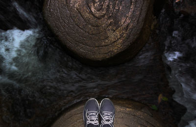 Low section of person wearing shoes on rock at river