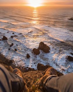Low section of person on beach against sky during sunset