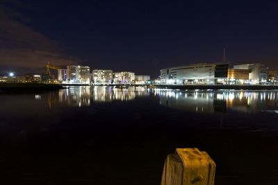 Illuminated city by sea against sky at night