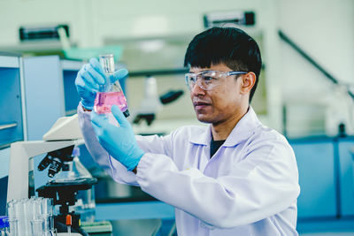 Asian male chemist wearing glasses and white lab working in laboratory