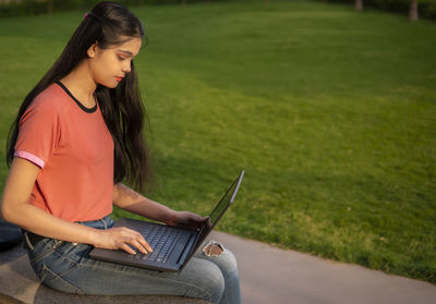 Young woman using laptop while sitting on field