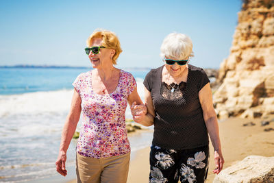 Two elderly women are walking along the rocky shore