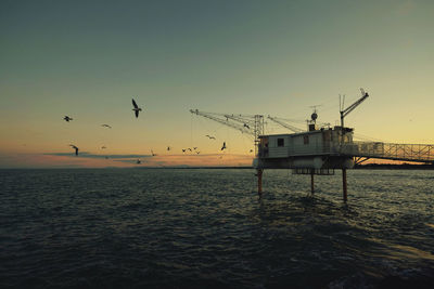 Drilling rig amidst sea against clear sky during sunset