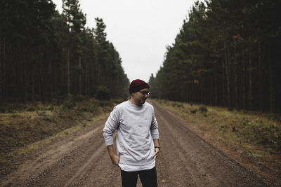 Man standing on dirt road in forest against clear sky