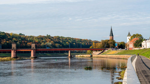 Bridge over river by buildings against sky