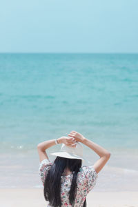 Rear view of woman with arms raised at beach against sky