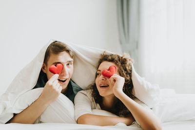 Romantic couple holding heart shapes while lying on bed at home