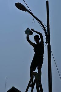 Silhouette man repairing street light against clear sky