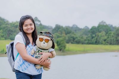 Portrait of smiling overweight woman holding toy while standing against lake